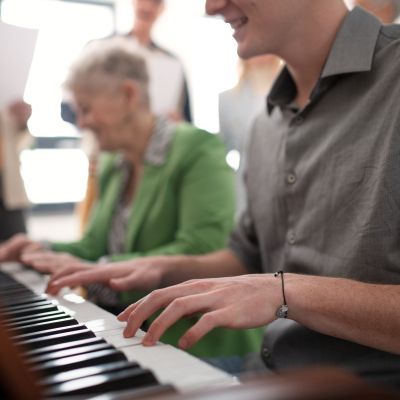 Two adult splaying the piano sat next to one another